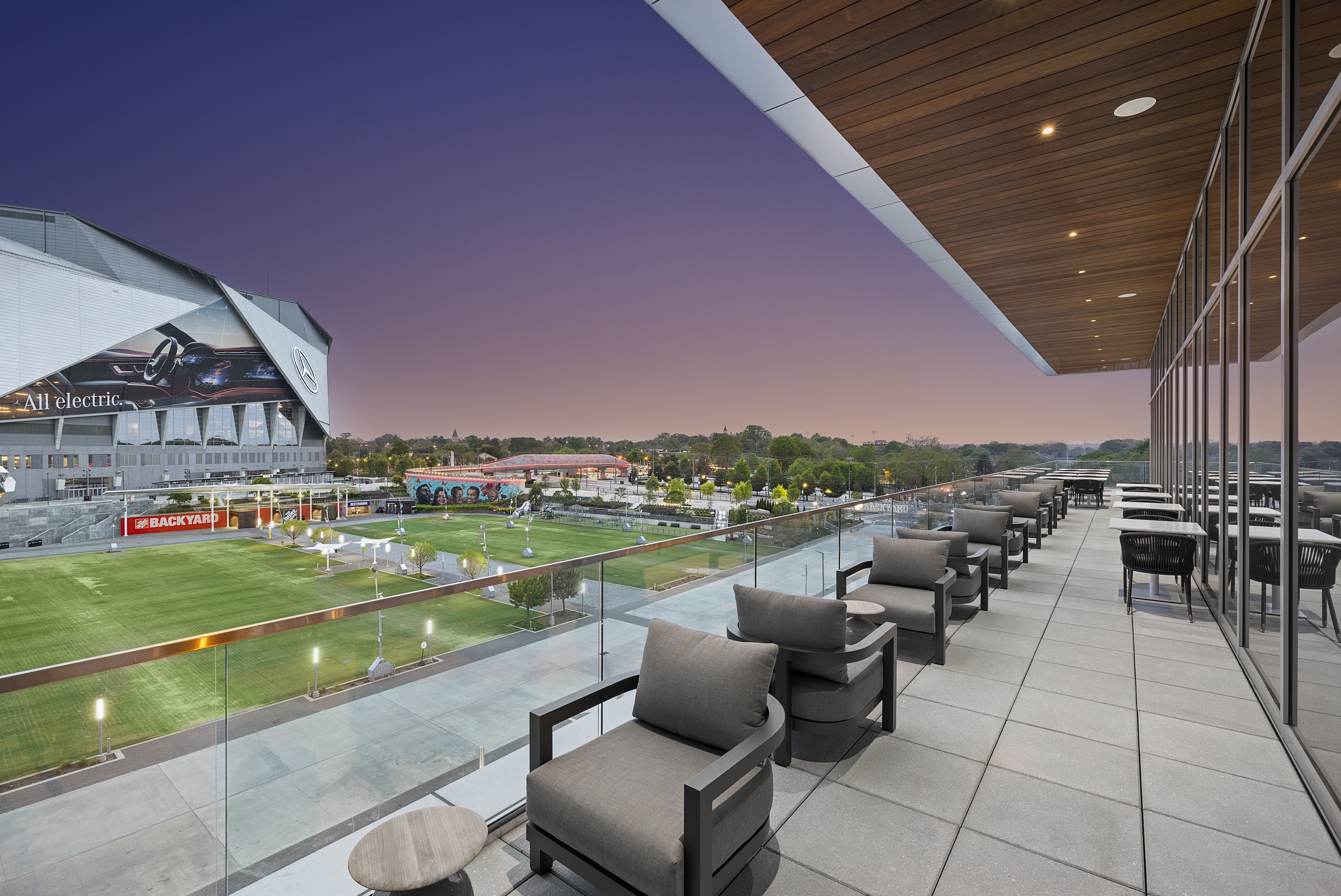 Upscale rooftop terrace overlooking a stadium in Atlanta, featuring modern seating and offering a panoramic view of the surrounding area at dusk, perfect for enjoying exquisite Italian dining under the stars.