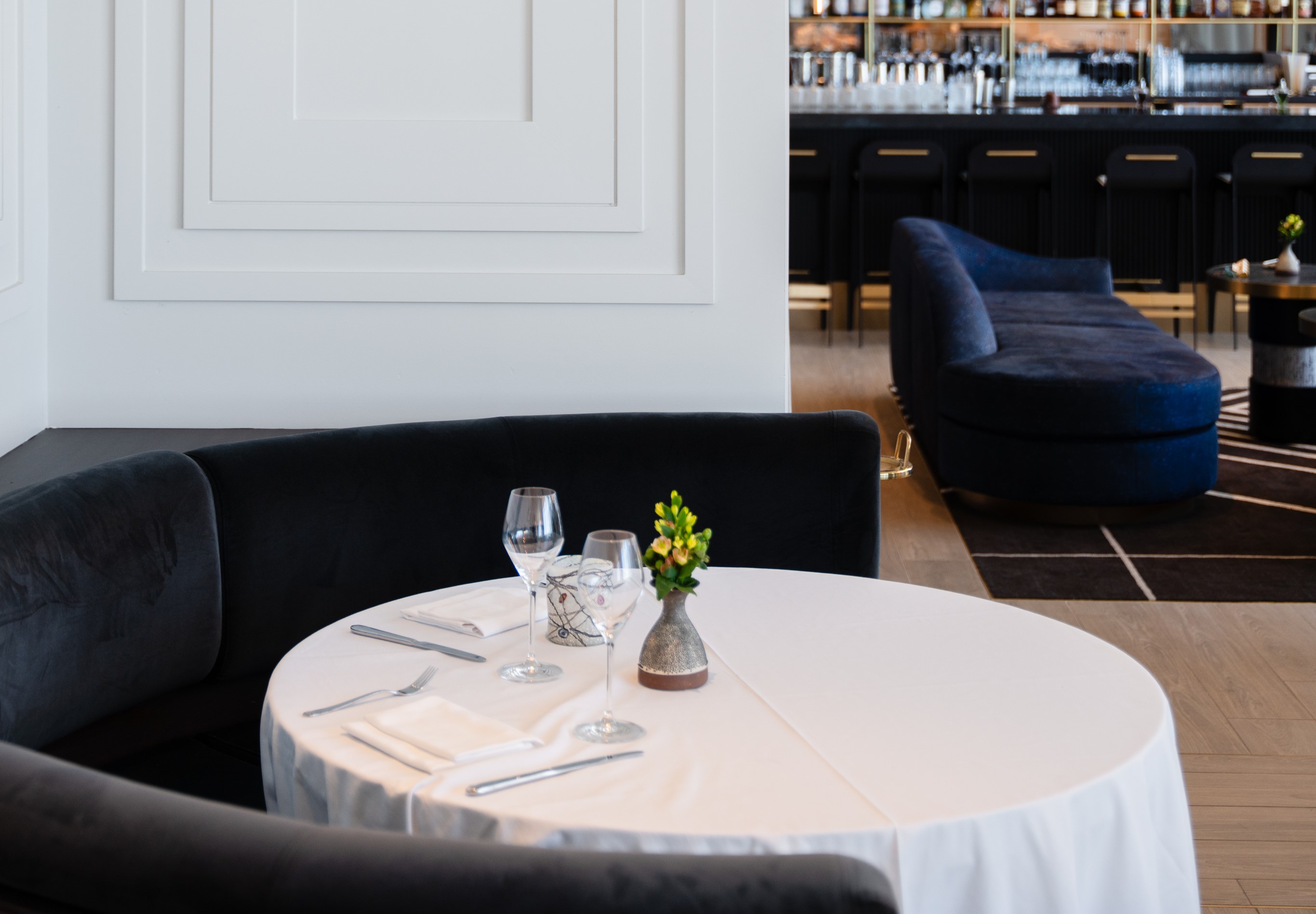 Elegant restaurant in Atlanta with a set dining table featuring a white tablecloth, wine glasses, folded napkins, and a small vase with yellow flowers. A curved black sofa surrounds the table, offering an inviting atmosphere for Italian dining.