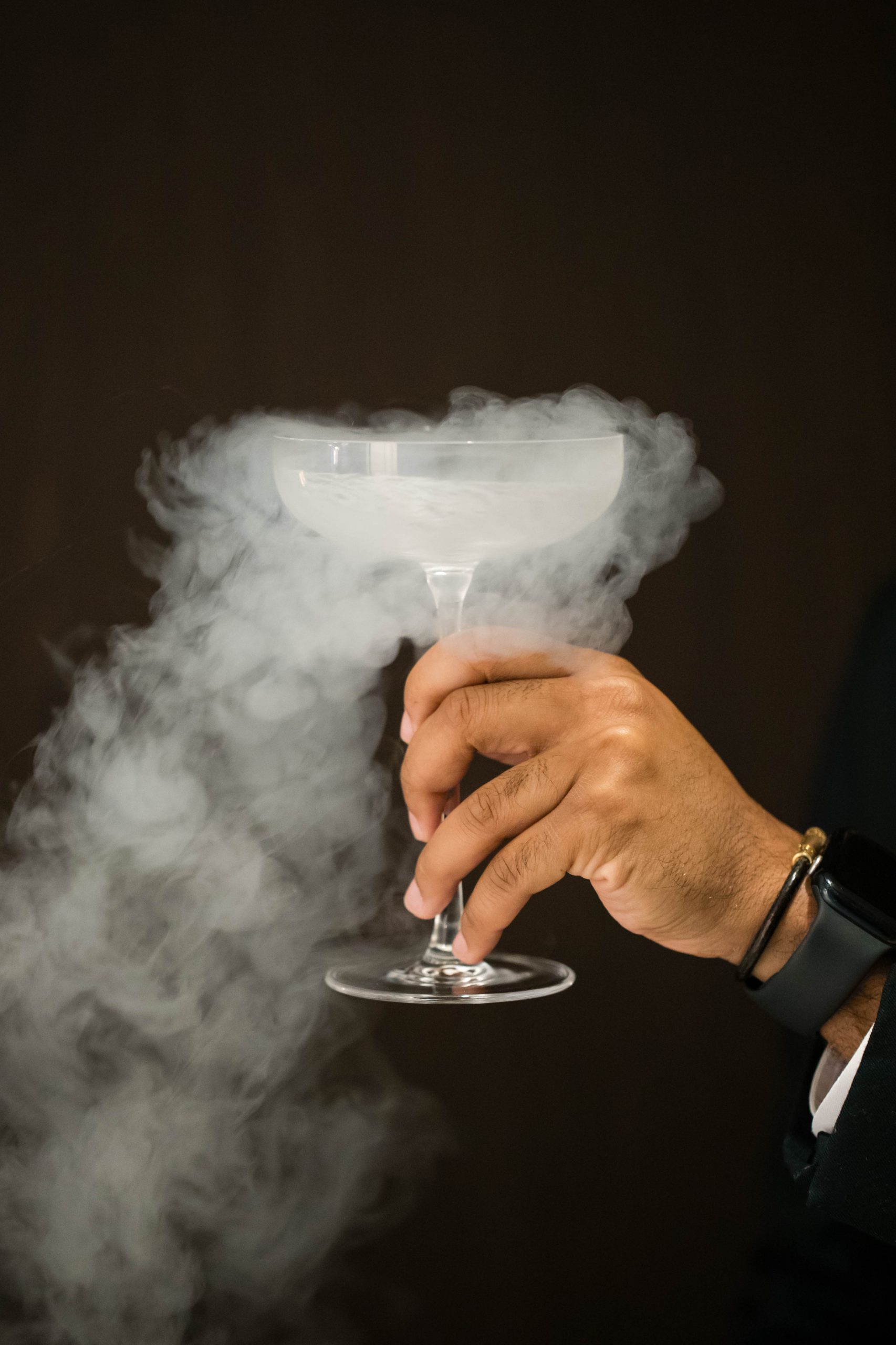 A hand holding a smoking cocktail glass filled with vapor against a dark background captures the allure of upscale Italian dining.