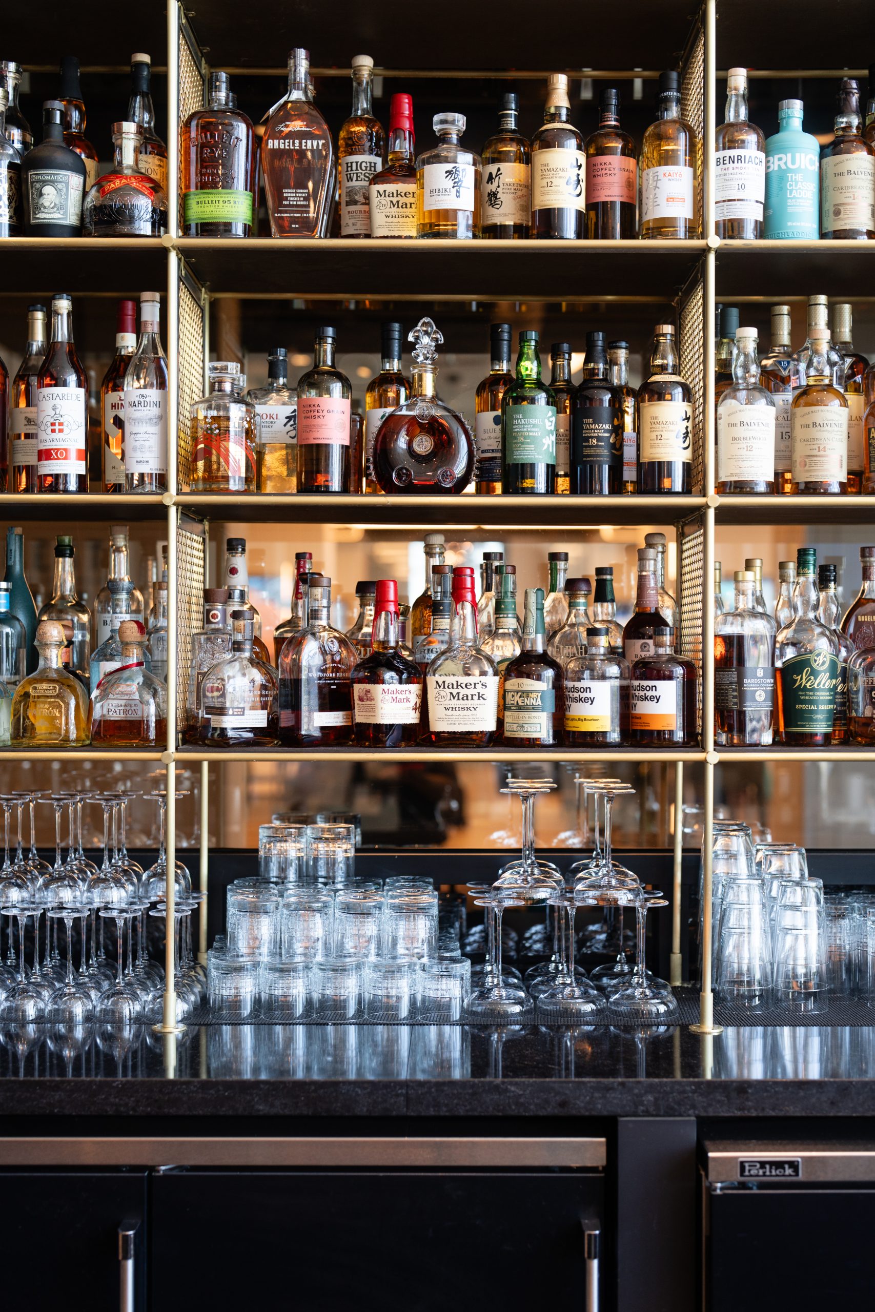 A well-stocked bar shelf displays various bottles of liquor at this upscale Italian restaurant in Atlanta, with rows of empty glasses arranged below.