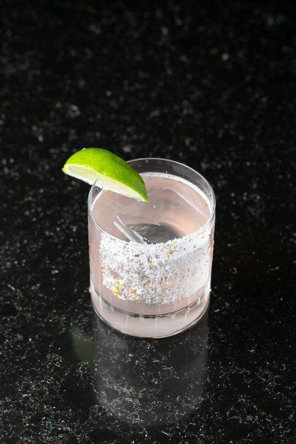 A cocktail in a glass with salt on the rim, a large ice cube, and a lime wedge garnish sits elegantly on a dark, speckled surface, capturing the essence of an upscale Atlanta restaurant.