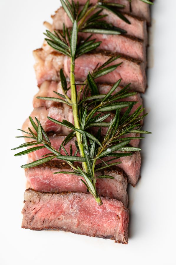 Sliced medium-rare steak garnished with fresh rosemary, showcasing a touch of Italian dining elegance, on a white background reminiscent of a fine restaurant experience in Atlanta.