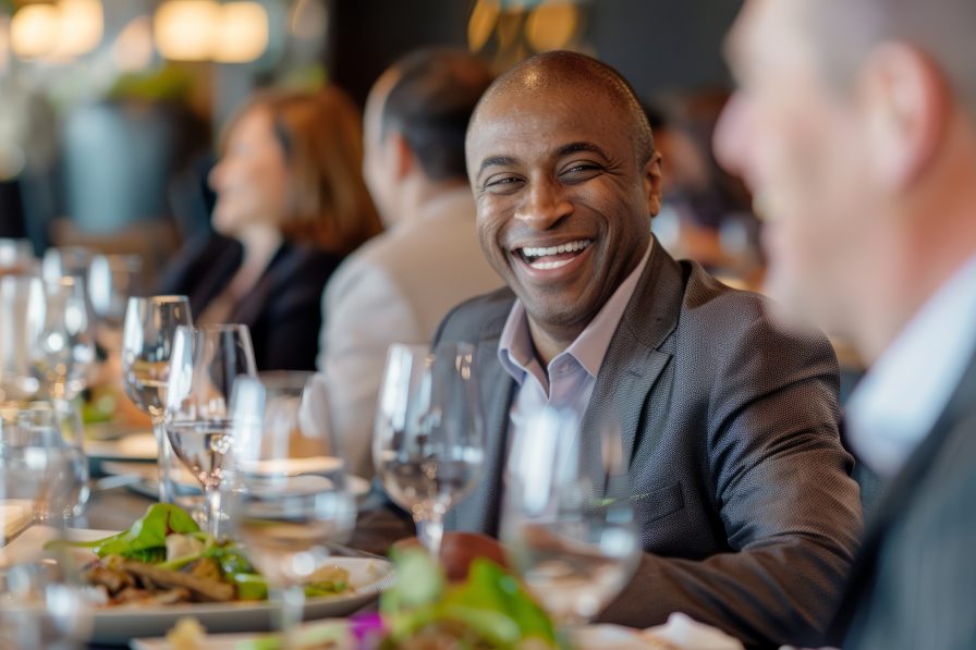 A smiling man in a suit sits among friends at an upscale restaurant in Atlanta, surrounded by plates and glasses.