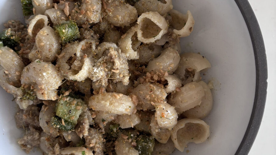 A bowl of orecchiette pasta mixed with pieces of green vegetables, ground meat, and sprinkled with grated cheese and seasonings.