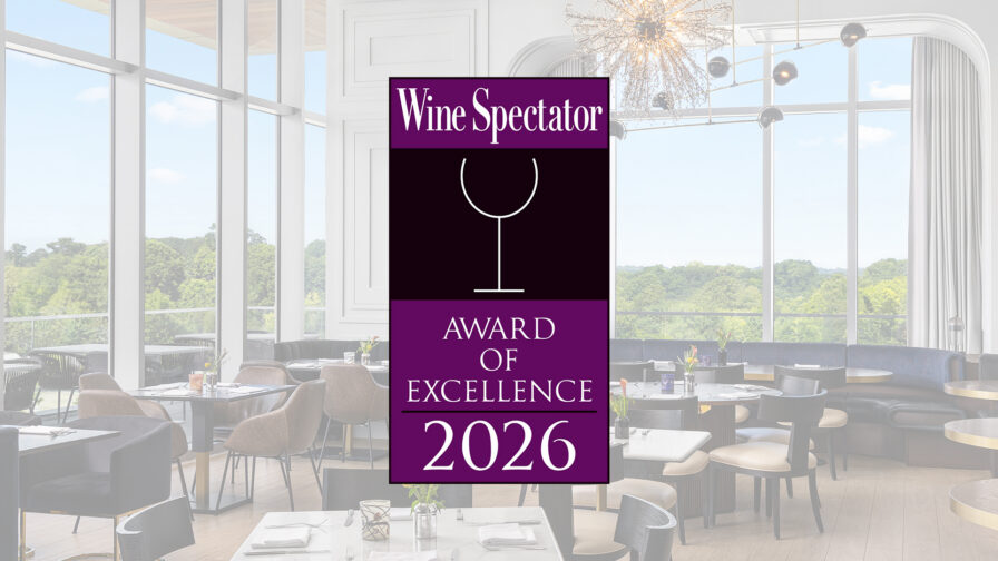 A restaurant dining room with large windows, featuring a "Wine Spectator Award of Excellence 2026" badge in the center.